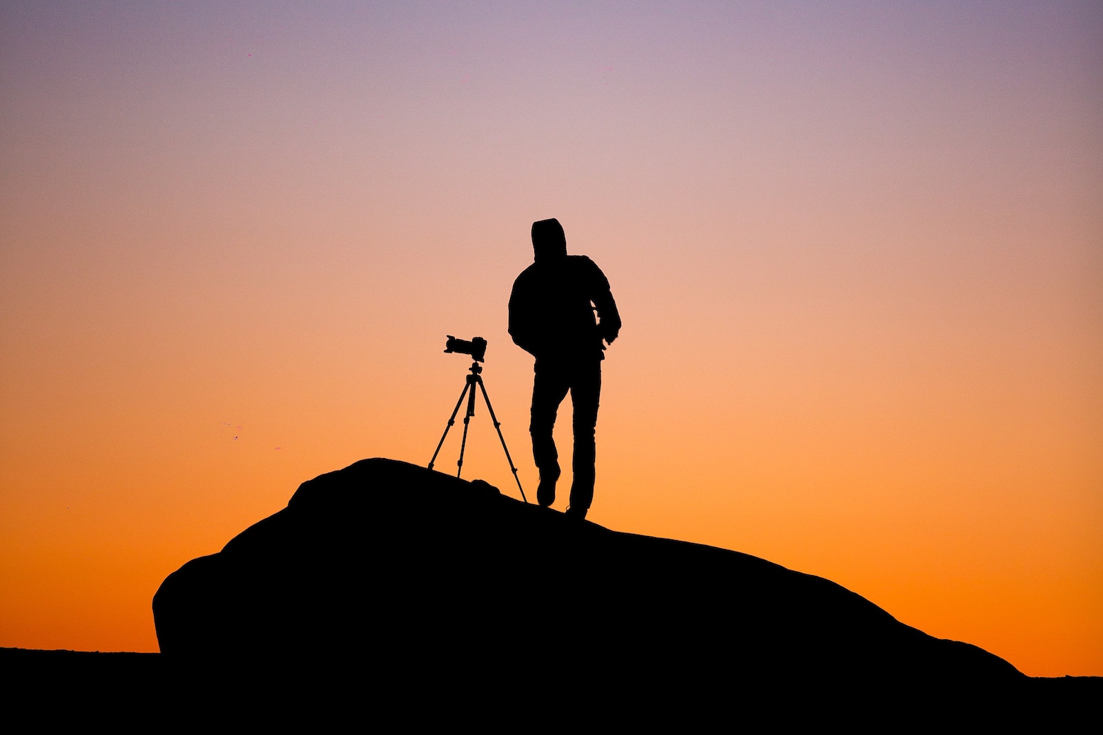 Silhouette of person standing beside camera at sunset